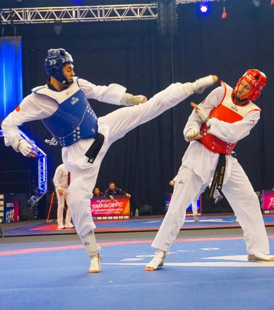 Two taekwondo fighters in action, one delivering a high kick.